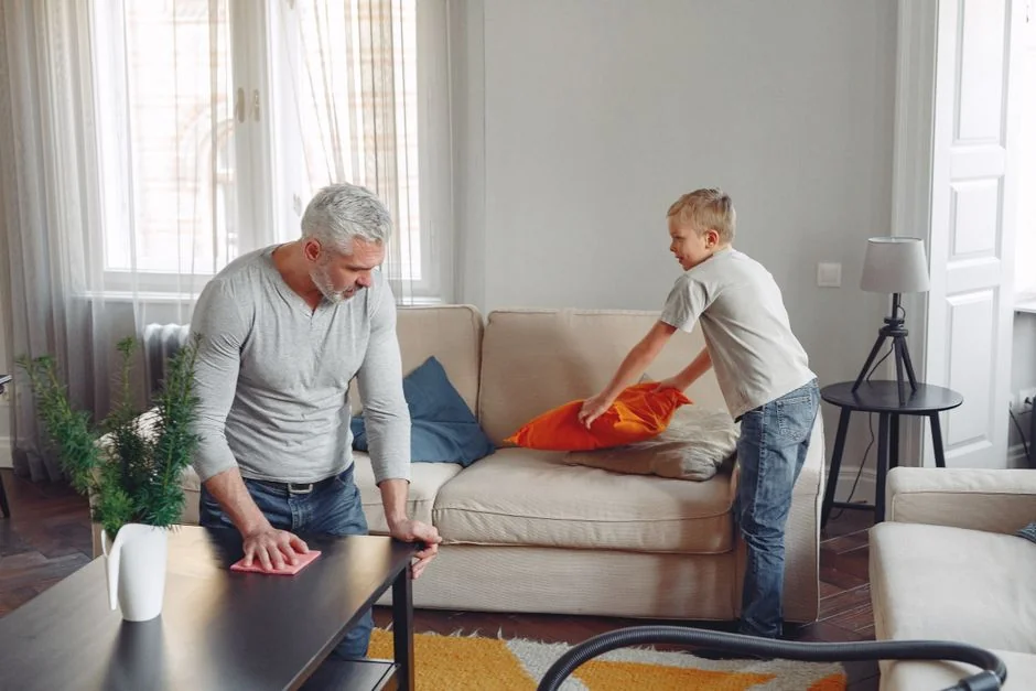 A professional cleaner in protective gear vacuuming the floor in a modern living room.